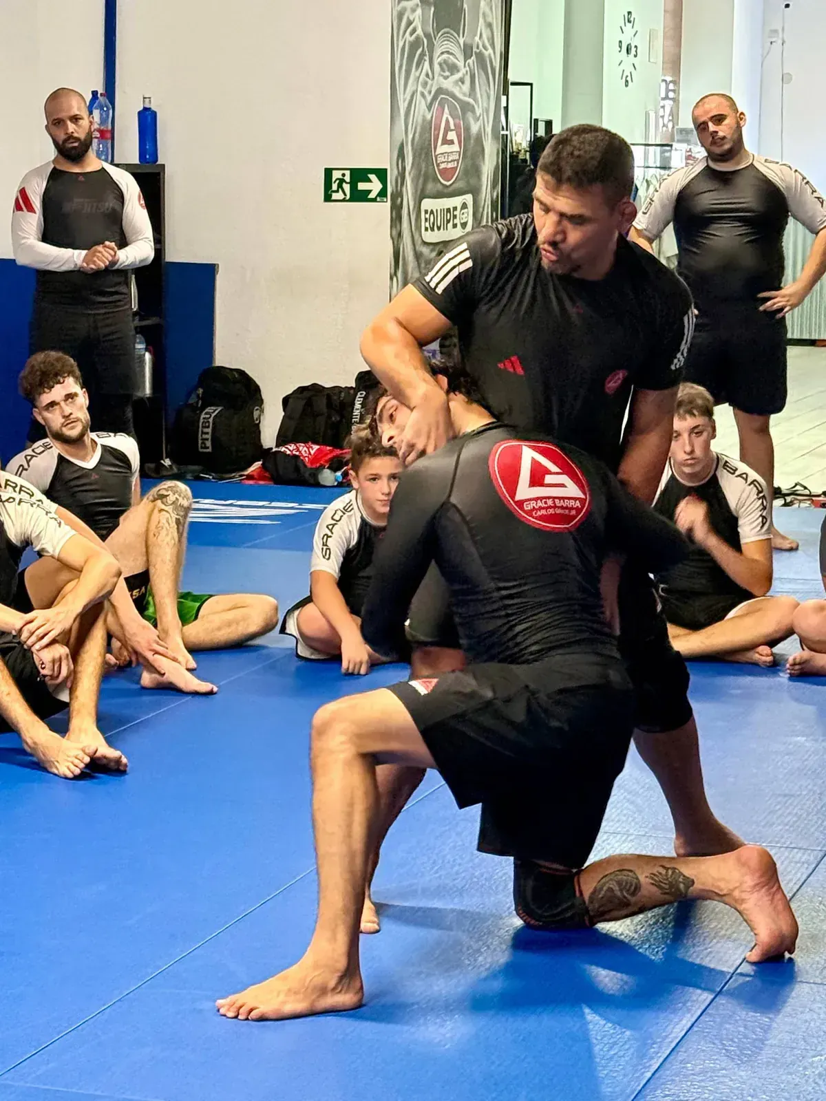 Instructor demostrando una técnica de Jiu-Jitsu rodeado por alumnos adultos